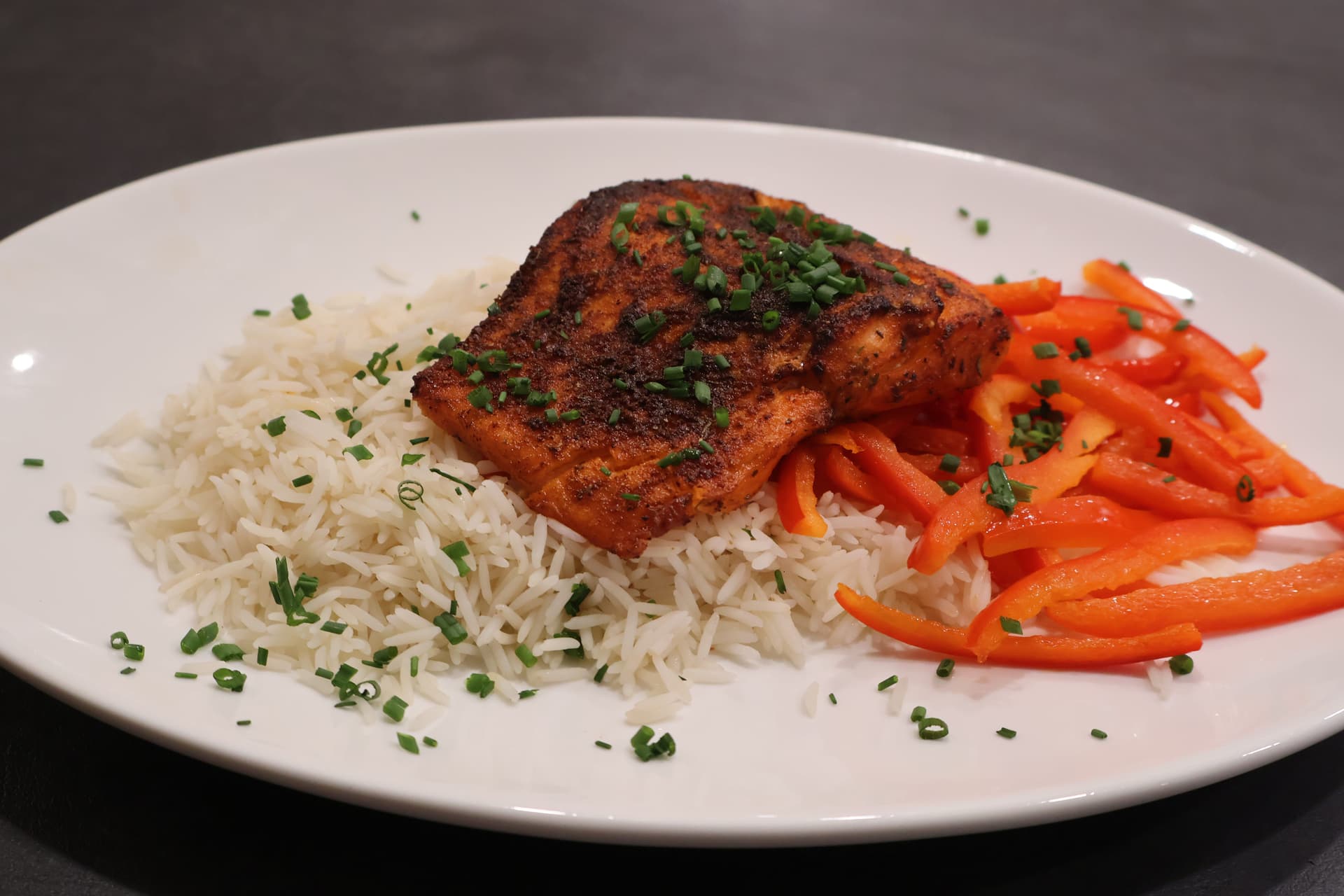 Air fryer salmon fillet with crispy skin served over white rice and red bell peppers, garnished with fresh chives.