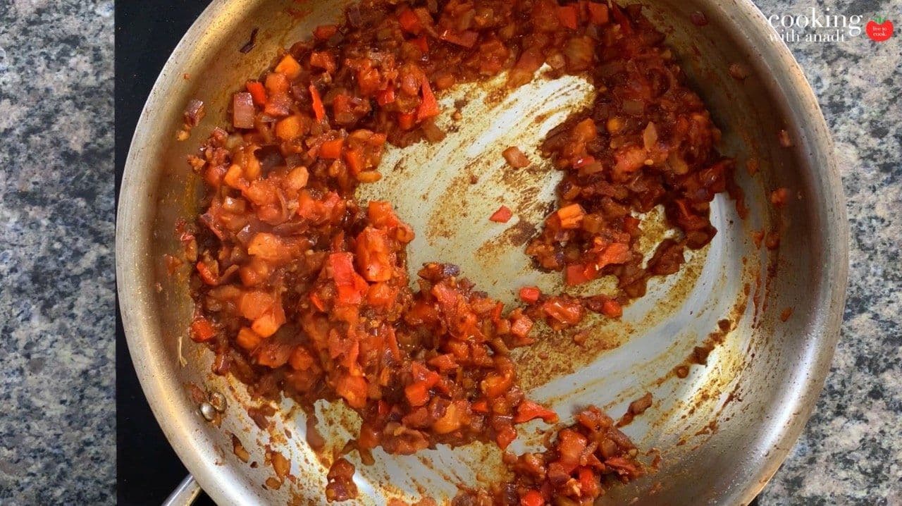 Diced red peppers and tomatoes sautéing in a pan with browned bits stuck to the bottom.