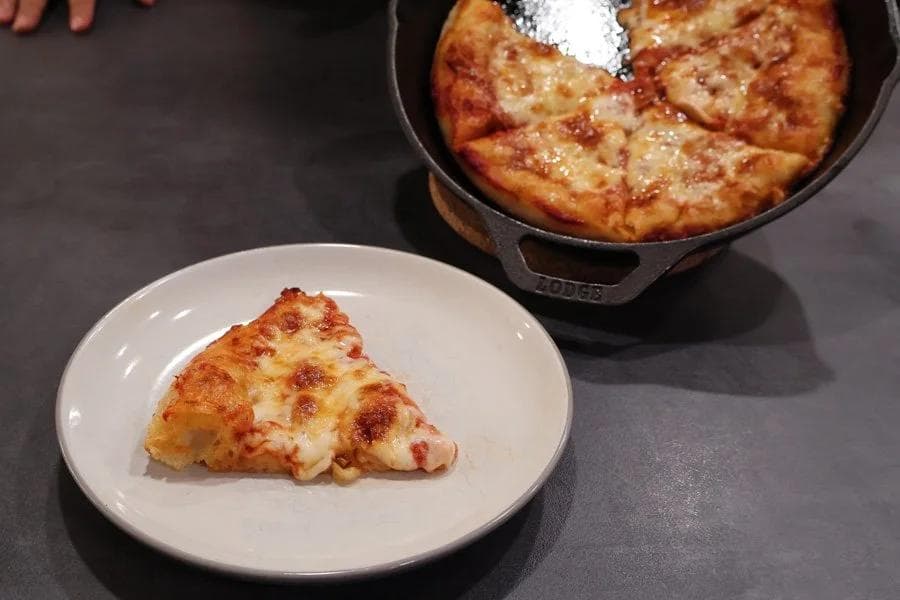 Cast iron pan pizza with one slice served on a white plate, showing golden-brown crust with melted cheese.
