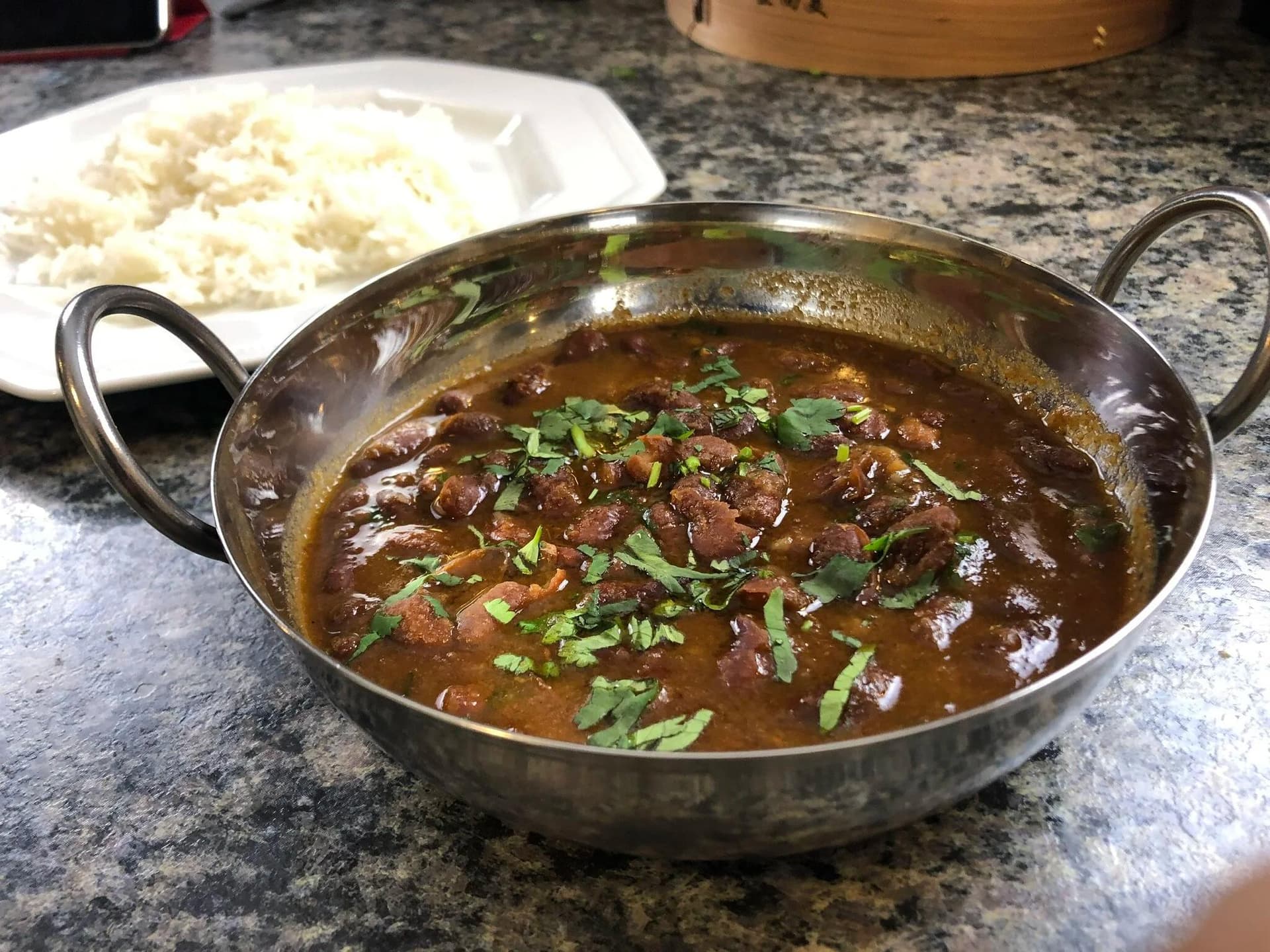 Rajma masala curry in a steel bowl garnished with cilantro, served with white rice on the side.
