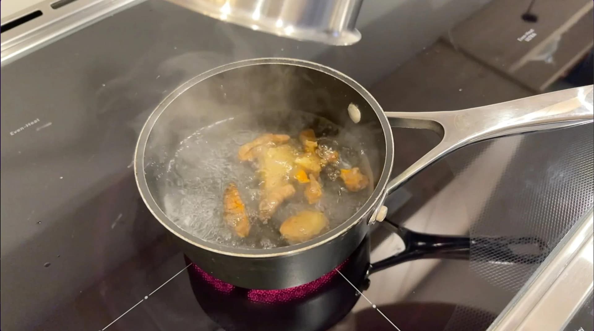Saucepan of boiling water with ginger and turmeric pieces simmering on stovetop.