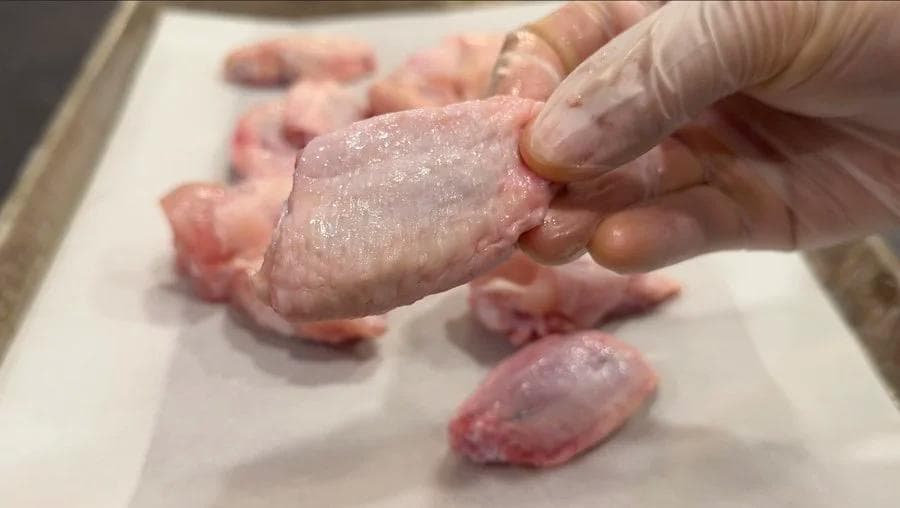 Hands patting raw chicken wings dry with paper towels on a white surface for air fryer preparation.