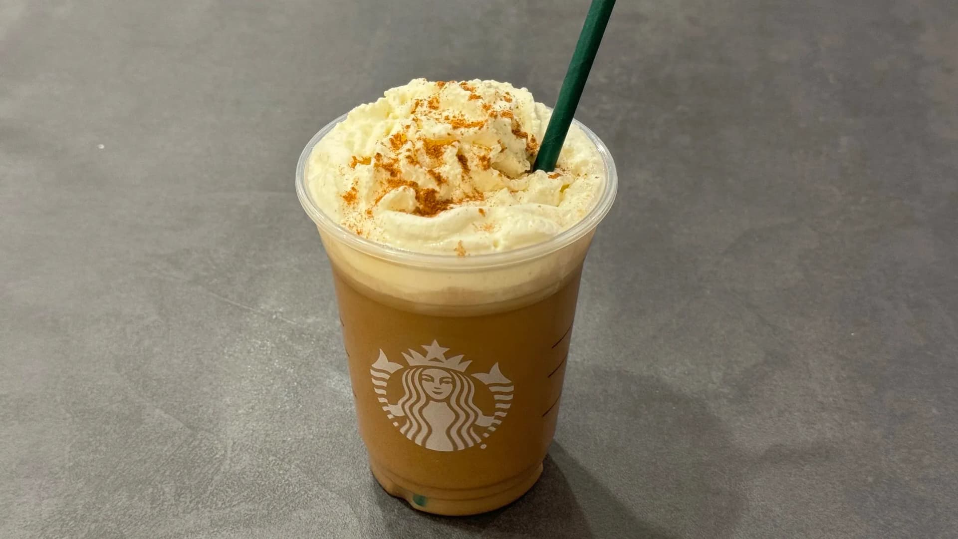 Iced Pumpkin Spice Latte topped with whipped cream and cinnamon sprinkle in a Starbucks cup.