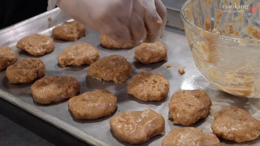 Raw chicken nuggets shaped and flattened on parchment paper before breading and air frying.