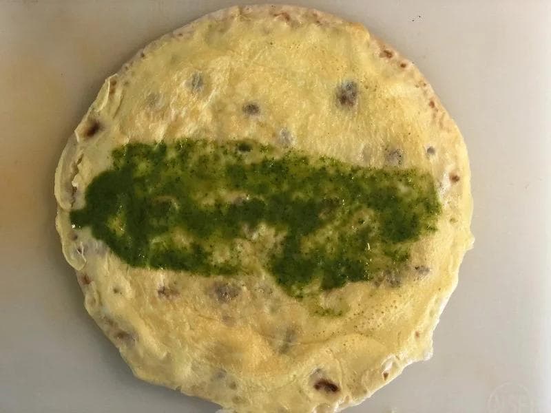 Cooked paratha with green mint chutney spread in a stripe across the center on a white surface.