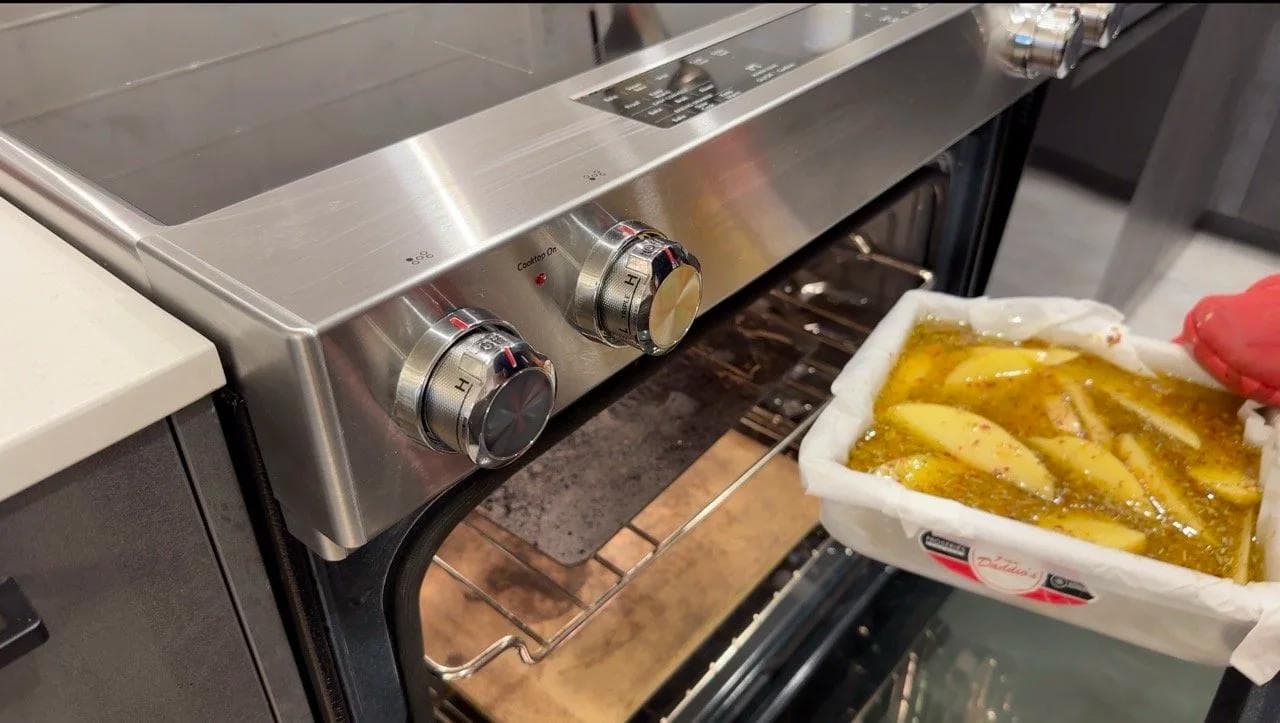 Baked Greek lemon potatoes in a white container beside an open oven with metal racks.