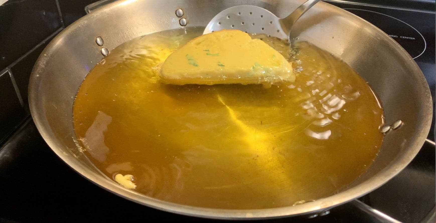 Battered bread pakora pieces frying in golden hot oil in a stainless steel pan with a slotted spoon.