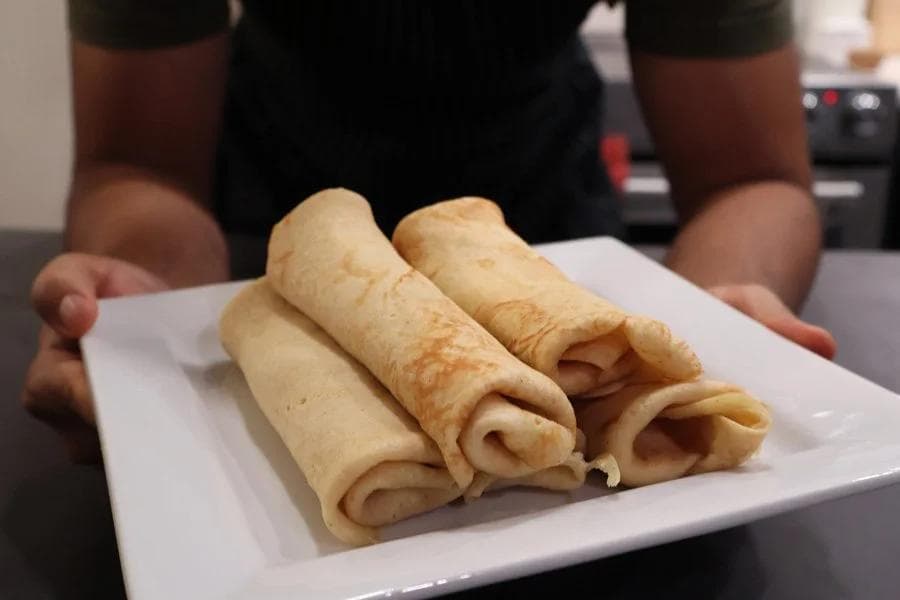 Four rolled pumpkin crepes arranged on a white plate, held by hands wearing a black shirt.