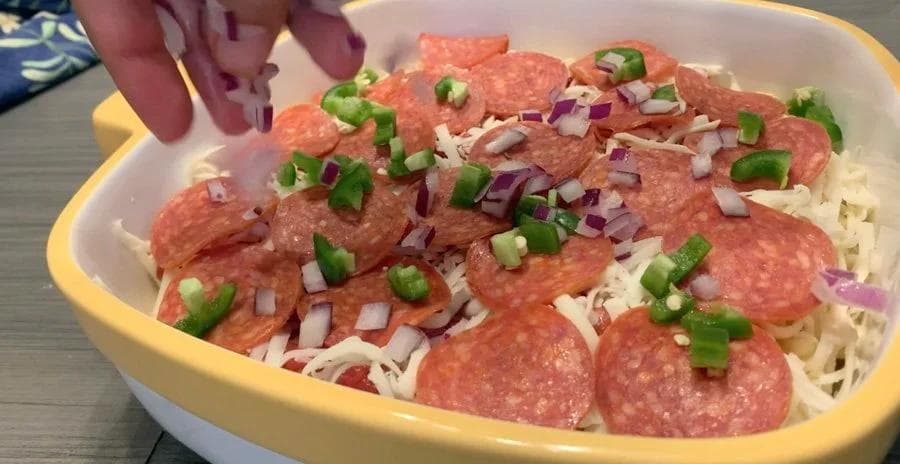 Pizza mac and cheese casserole topped with pepperoni slices, melted mozzarella, diced red onions, and green peppers.