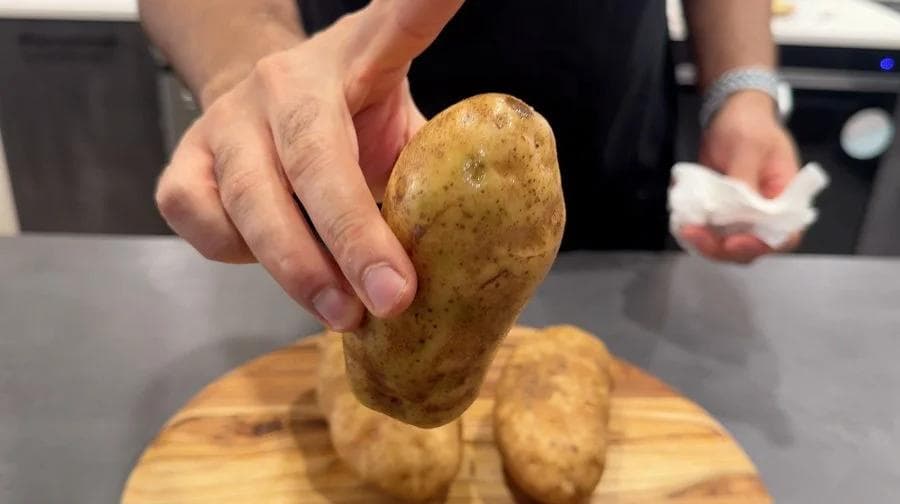 Hand holding a cooked potato above others on a wooden board, demonstrating air fryer baked potato results.