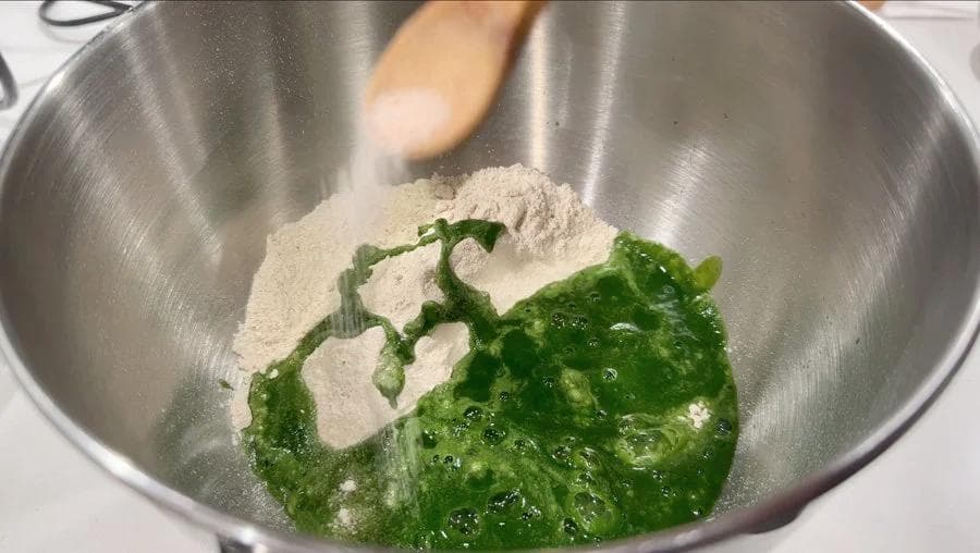 Spinach and atta flour being combined in a stainless steel bowl for palak paratha dough.