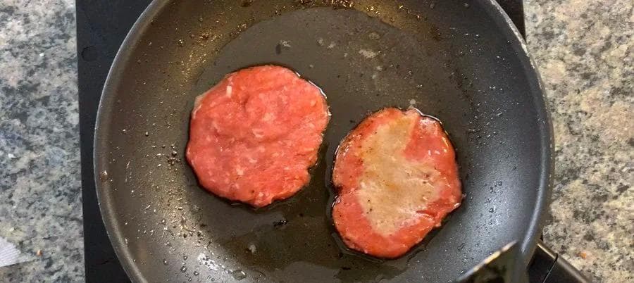 Two sausage patties cooking in a dark skillet, lightly browned on both sides.