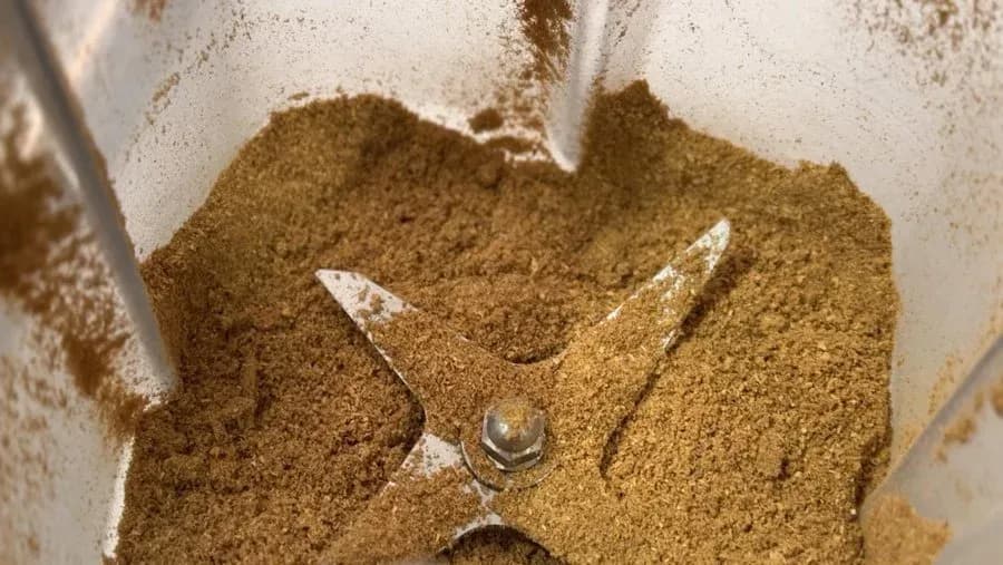Ground coriander spice in a white mortar and pestle with metal grinding blade.
