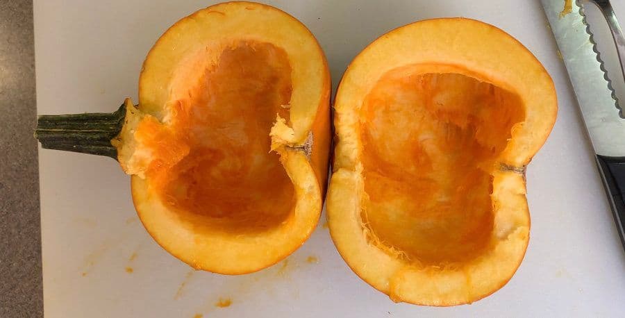 Two pumpkin halves with seeds and fibers removed, ready for roasting on a baking sheet.