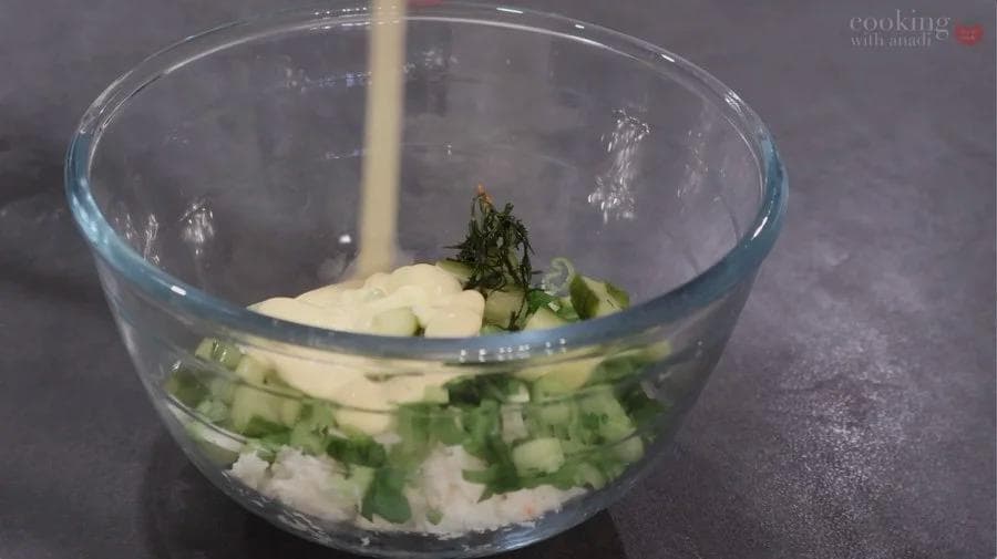 Crab salad ingredients mixed in a glass bowl with mayonnaise being added.
