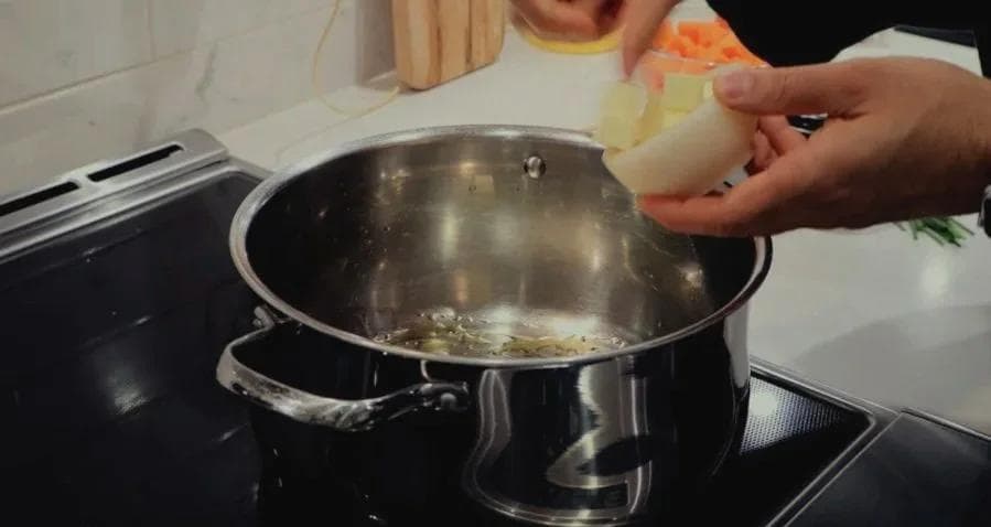 Hand pouring diced onions into a pot with melted butter and oil on the stovetop.