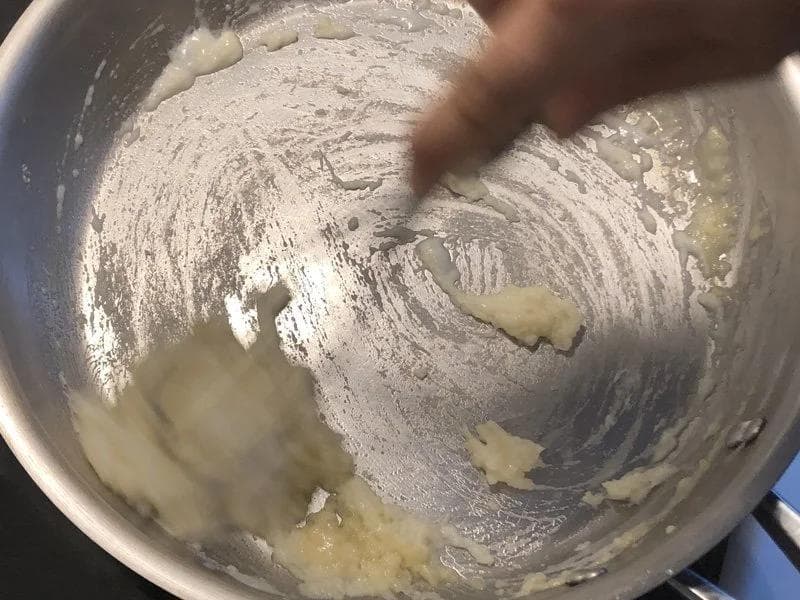 Whisking milk into a butter and flour roux in a metal pot to make béchamel sauce