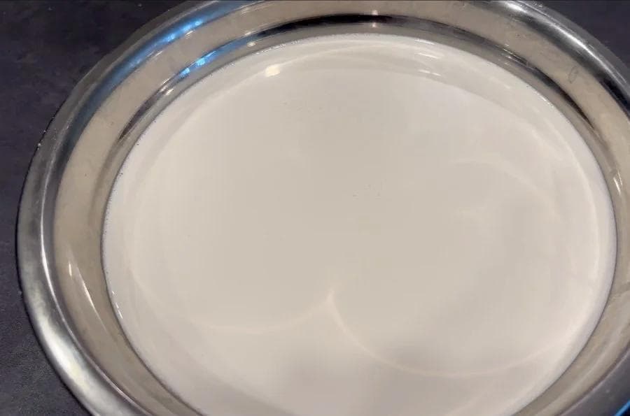 Freshly strained almond milk in a glass bowl lined with cheesecloth, showing smooth white liquid.