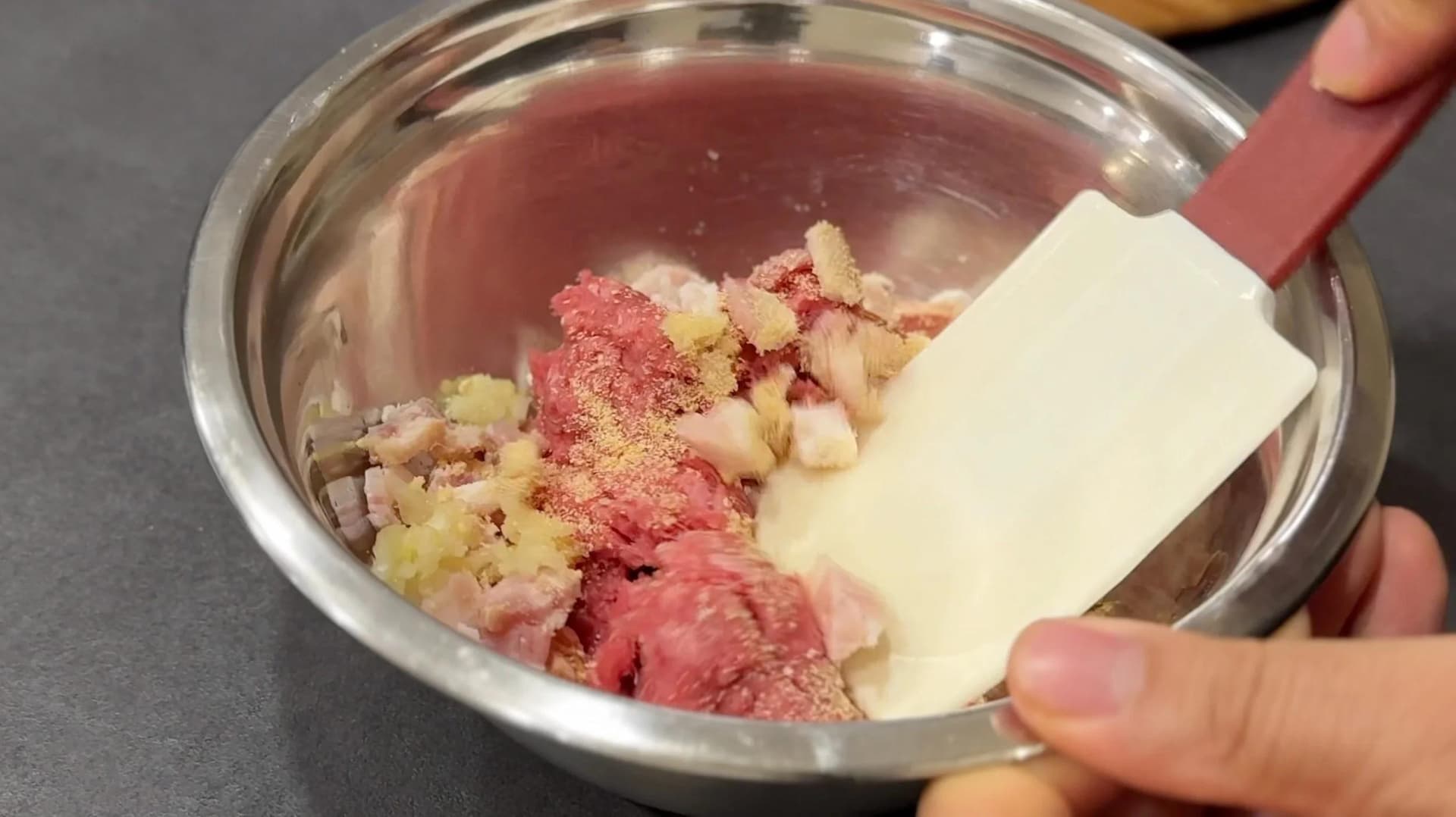 Ground beef mixed with bacon, garlic, and onion powder in a bowl with a spatula, ready to form slider patties.