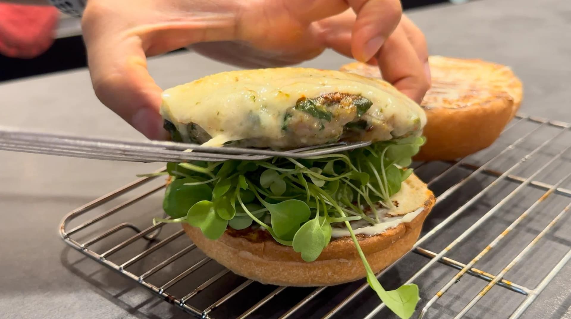 Hands assembling a spinach turkey burger with melted cheese, fresh arugula, and toasted bun.