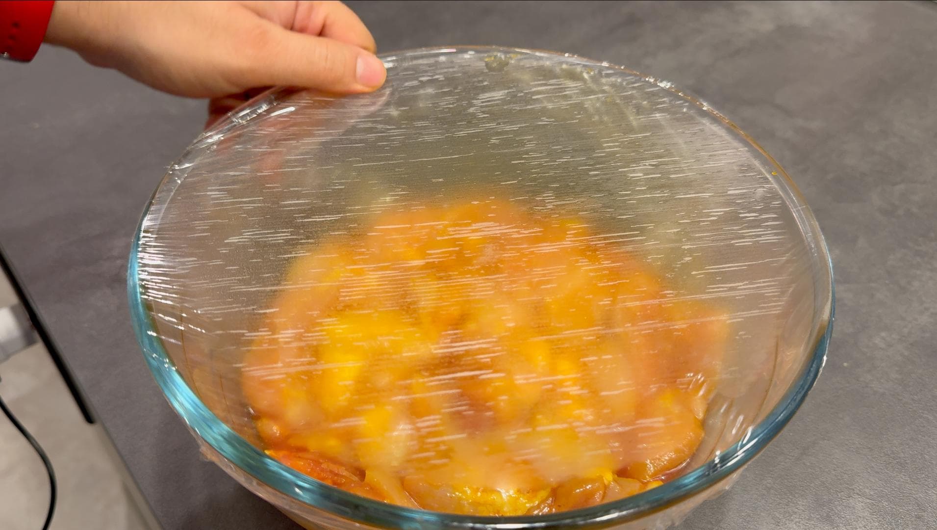 Chicken pieces marinating in saffron-infused water in a glass bowl covered with plastic wrap.