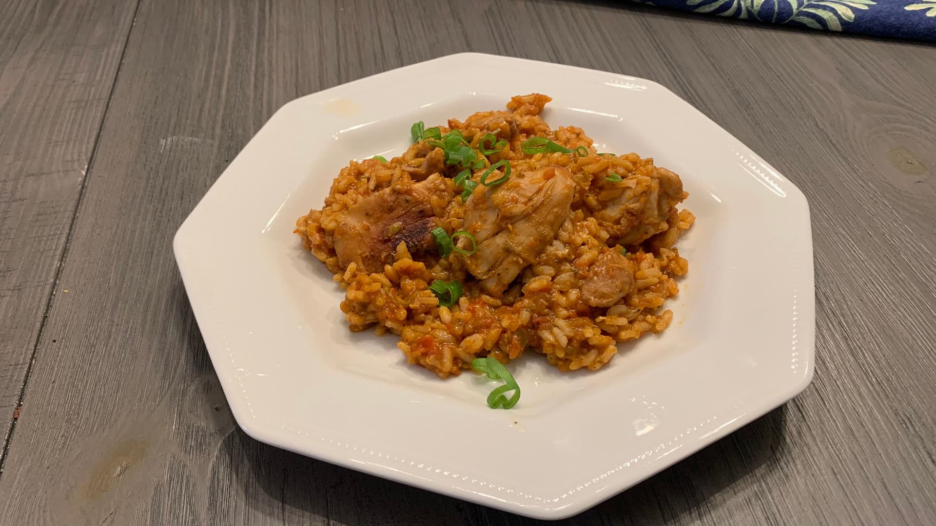 Finished Arroz Con Pollo served on a white plate, featuring chicken and yellow rice garnished with green onions.