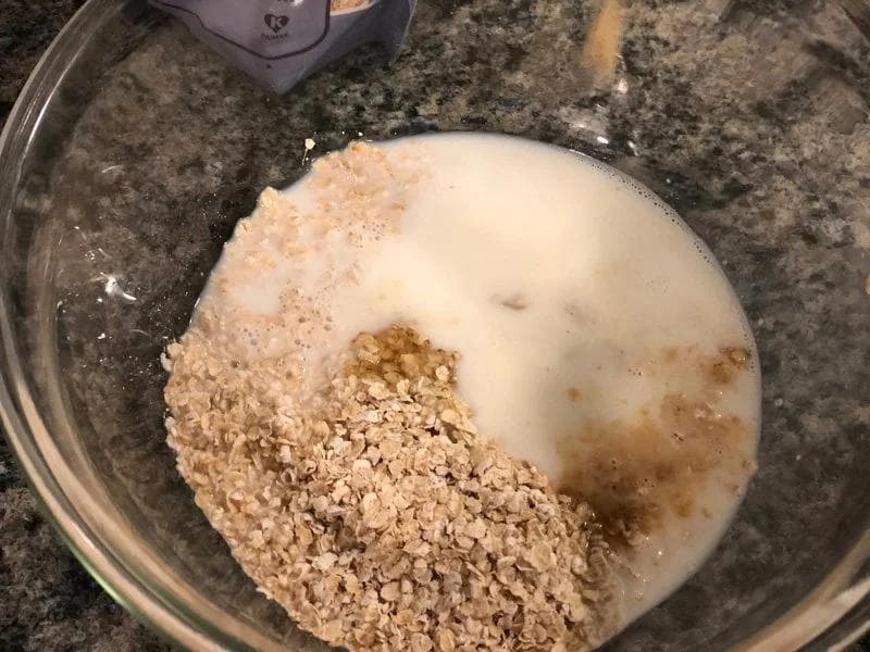 Overnight oats ingredients in a glass bowl: oats, milk, cocoa powder, and mashed banana.