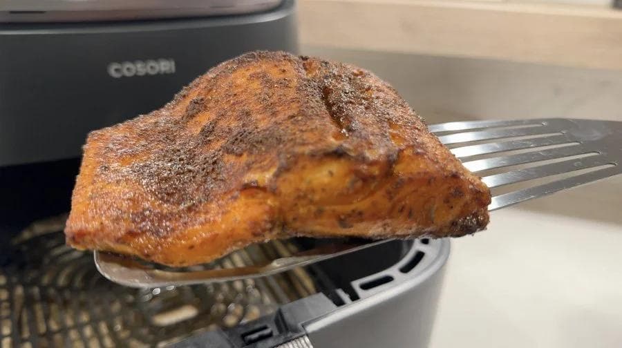 Cooked salmon fillet with crispy skin on a fork, dusted with seasoning, fresh from the air fryer.