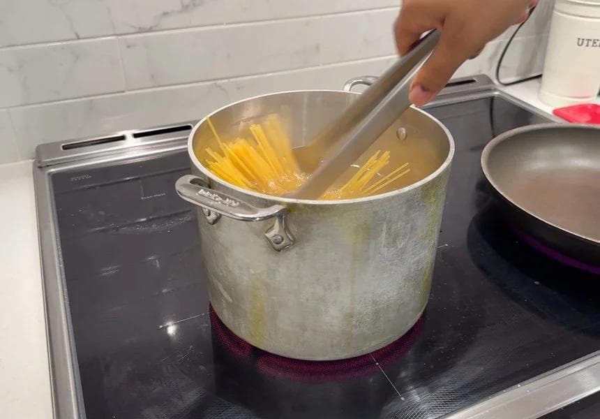 Pasta being stirred in a large pot of boiling water with a wooden spoon on a stovetop.