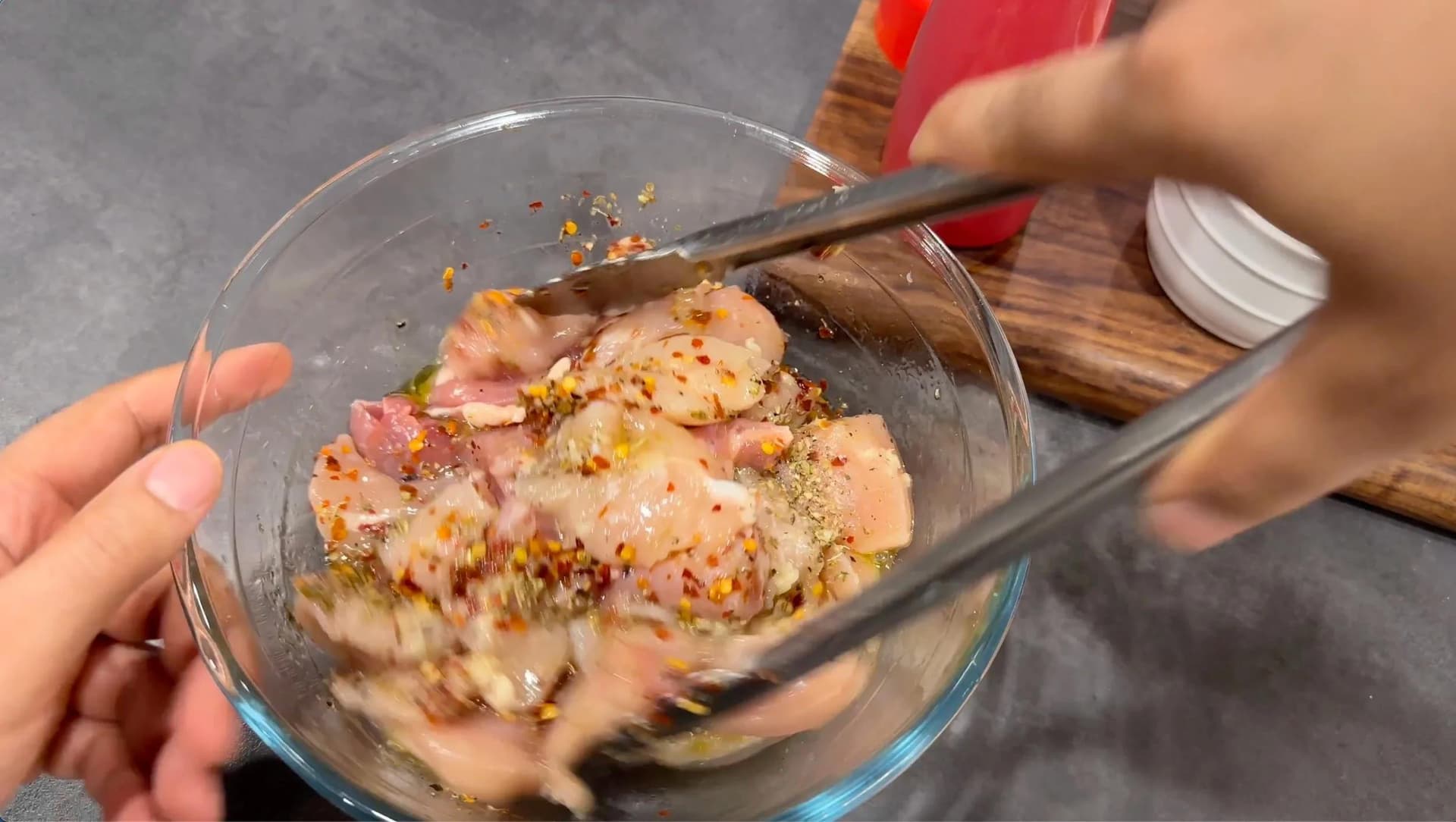 Marinated chicken cubes coated in olive oil, lemon juice, garlic, and herbs being mixed in a glass bowl with a spoon.