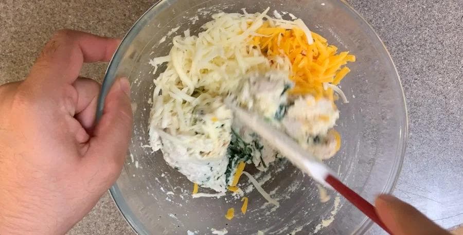 Mixing ricotta, spinach, shredded cheddar cheese, and other ingredients in a bowl with a spatula.