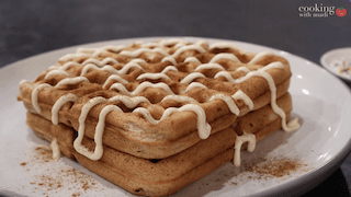 Stacked sugar cookie waffles drizzled with white icing and dusted with cinnamon on a white plate.