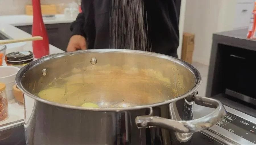 Large pot of simmering golden broth with softened onions and aromatics being stirred in a kitchen.