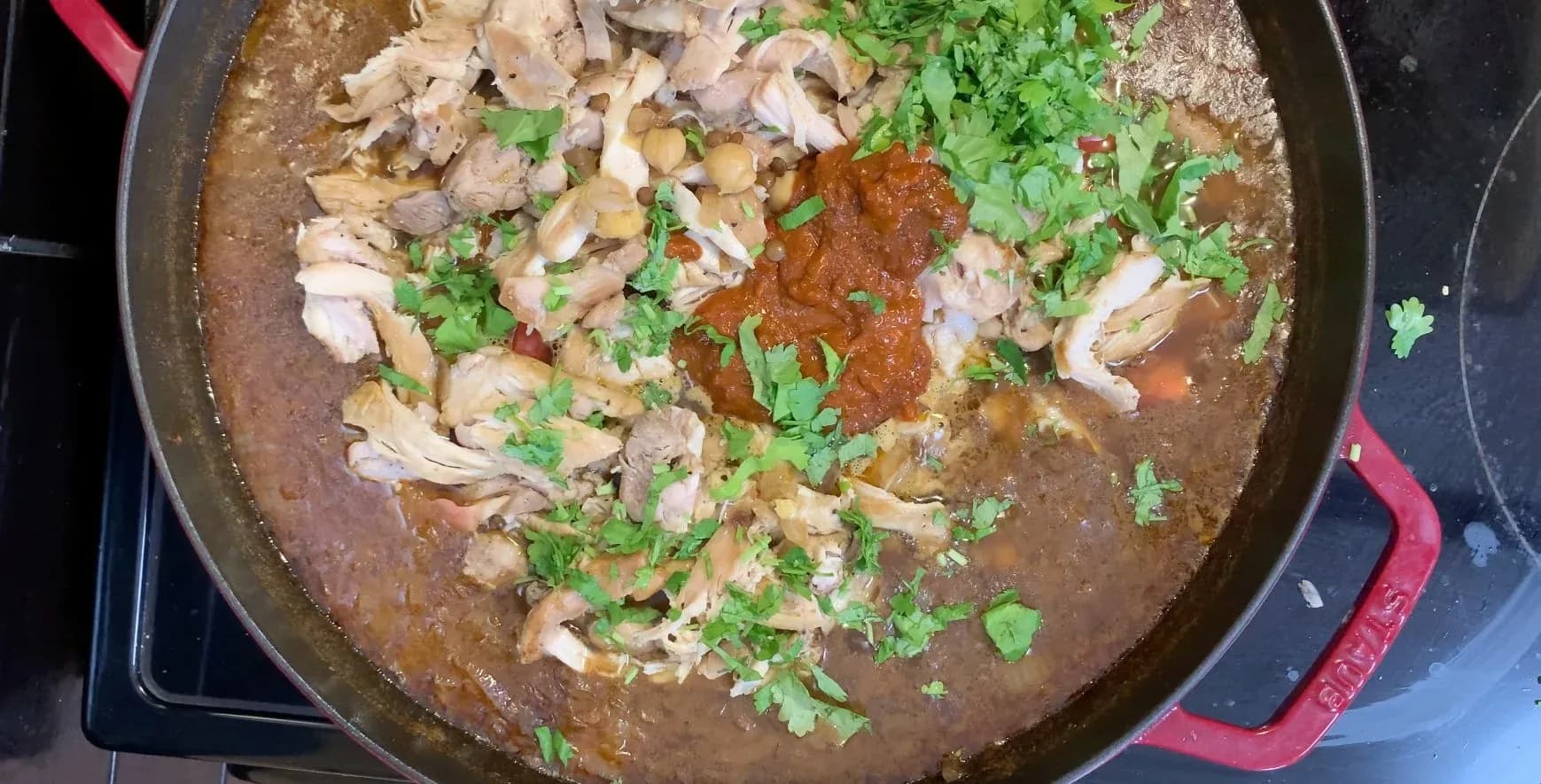Moroccan chicken and chickpea stew in a red Dutch oven with shredded chicken, fresh cilantro, and rich brown broth.