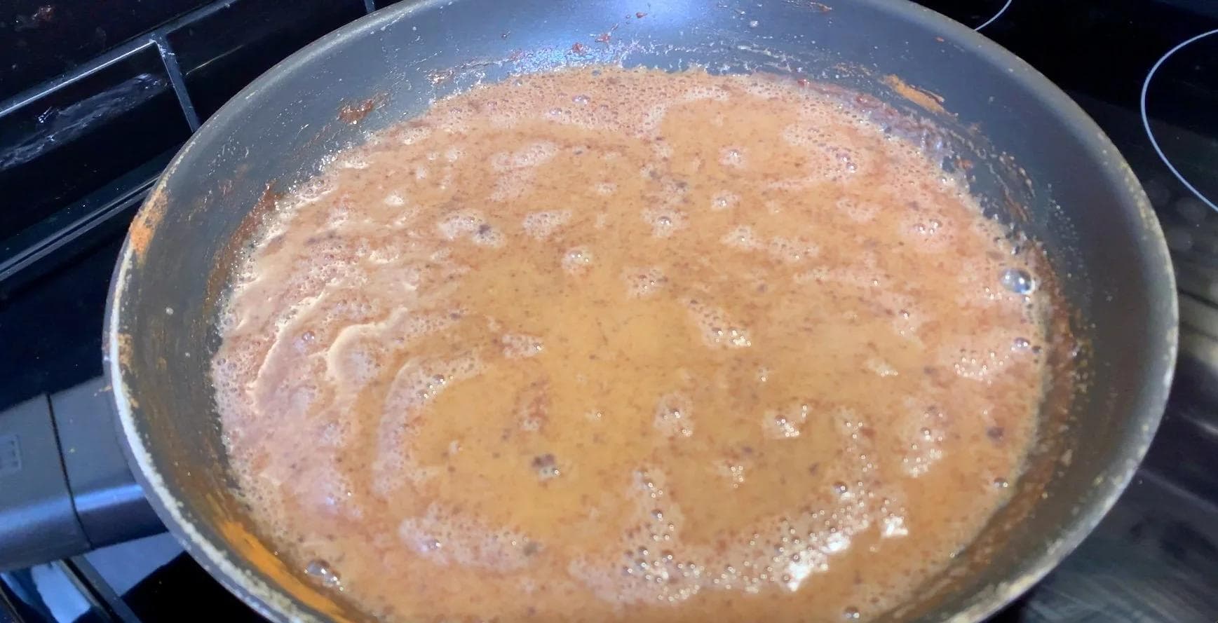 Pumpkin spice syrup simmering in a saucepan, showing a tan-colored mixture with bubbles forming on the surface.