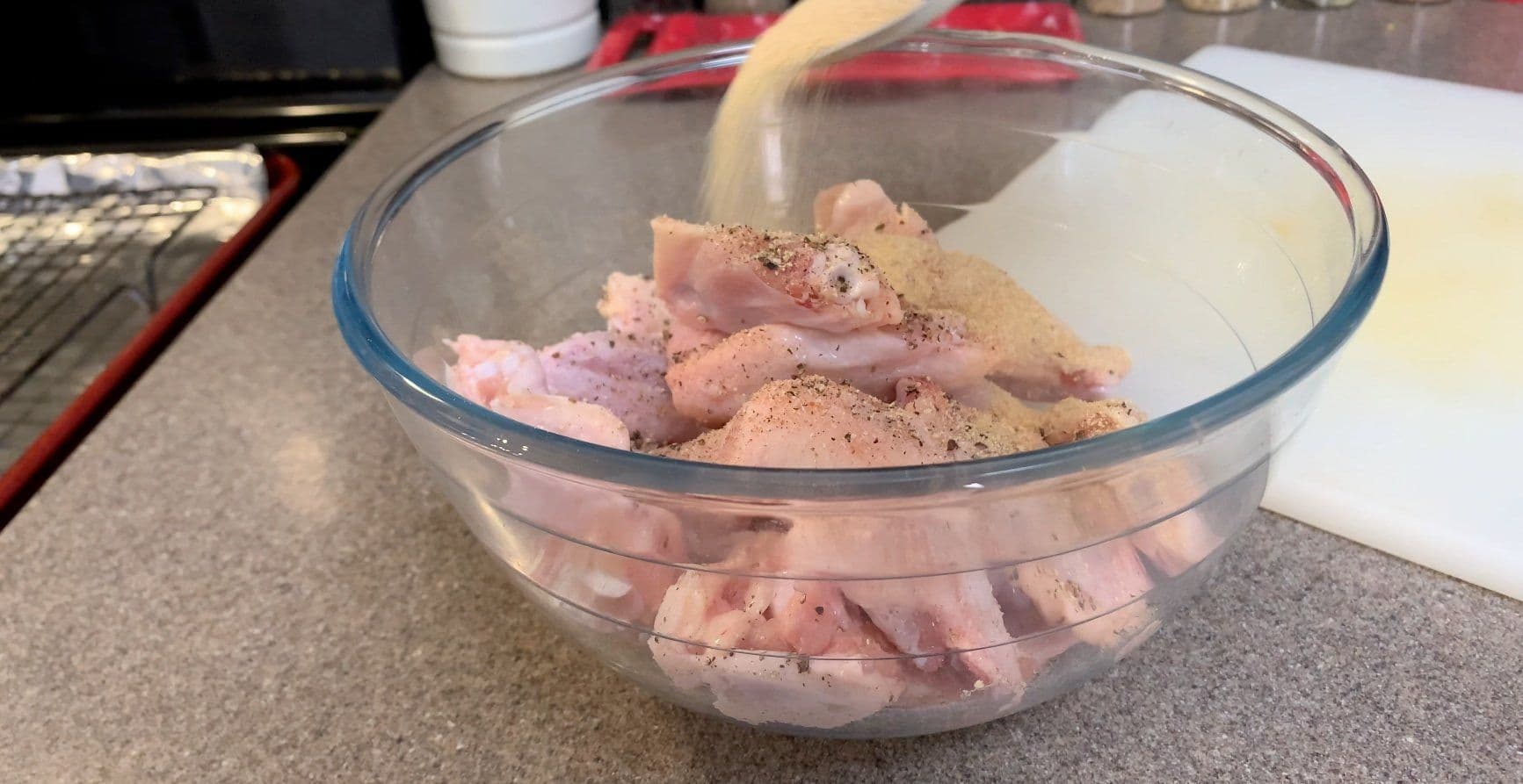 Raw chicken wings seasoned with garlic powder, salt, pepper, and flour in a glass bowl before air frying.