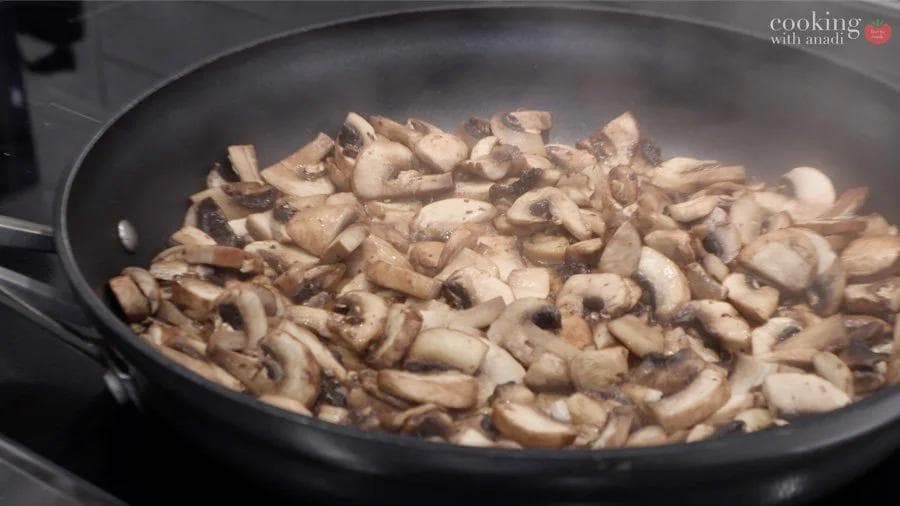 Sliced mushrooms sautéing in a dark pan, partially cooked and reduced in volume.