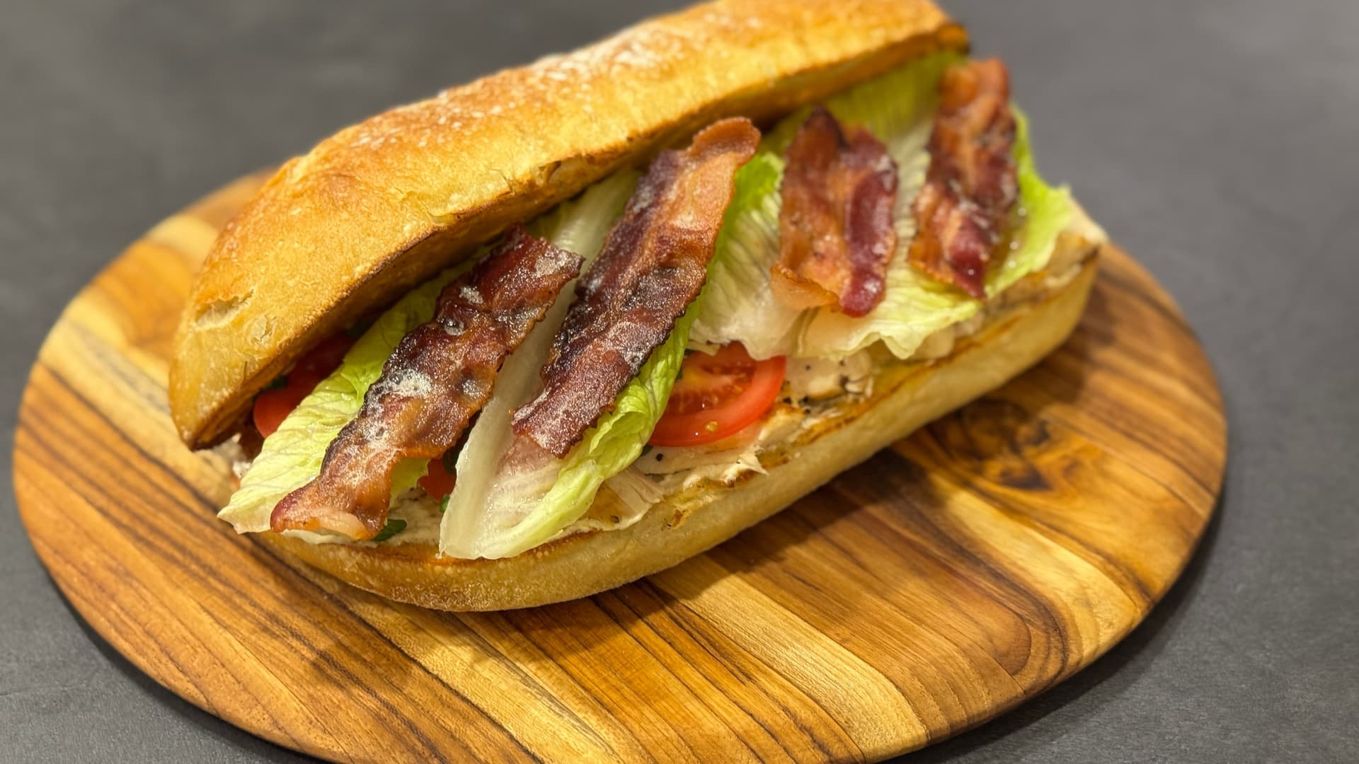 BLT sandwich with crispy bacon, lettuce, tomato, and mayo on toasted bread, served on wooden board.