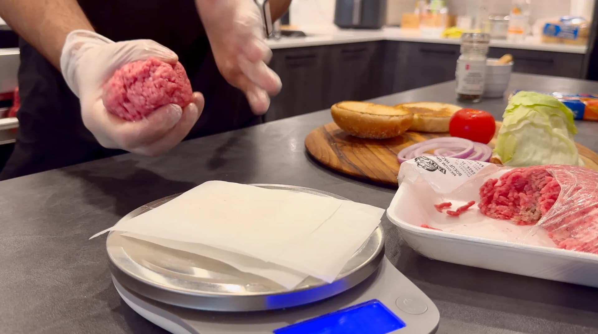 Chef forming ground beef portions into smooth balls for burger patties above parchment paper squares.