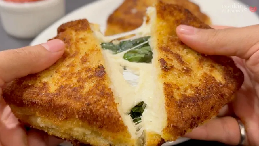 Mozzarella in Carrozza cut diagonally in half, showing melted cheese and basil between golden-brown fried bread.