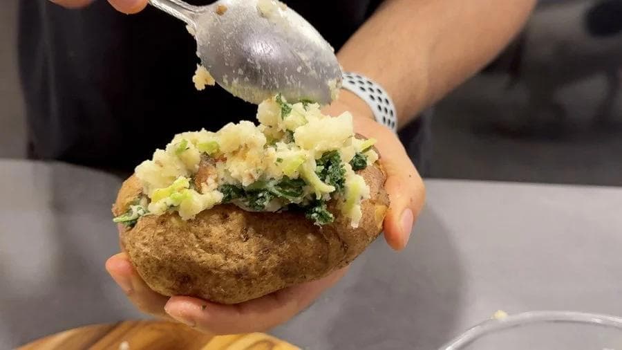 Hands spooning colcannon filling into a baked potato shell in an air fryer twice baked potato recipe.