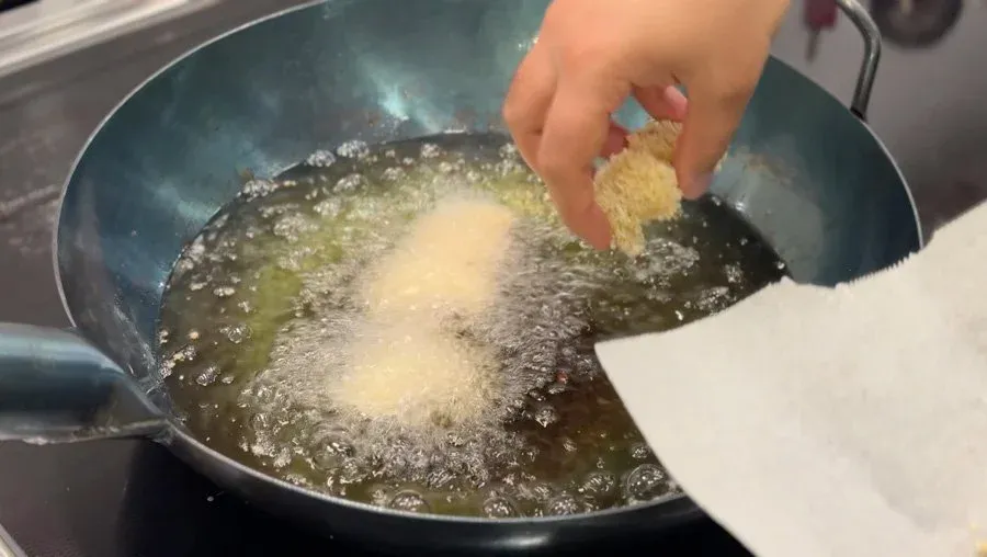 Hand dropping breaded shrimp into hot oil in a wok for deep frying.