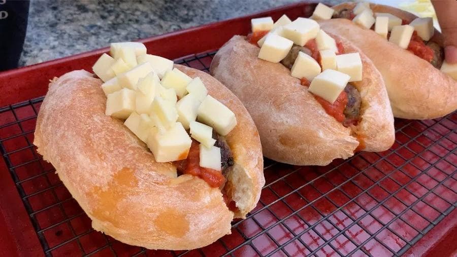 Italian meatball subs topped with cubed mozzarella and provolone cheese on a red baking sheet.