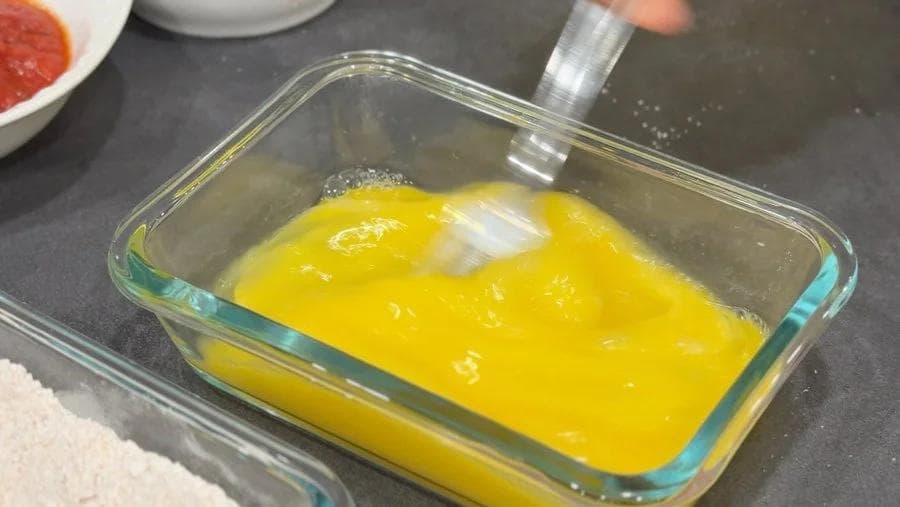 Whisked eggs in a glass baking dish for coating shrimp during popcorn shrimp preparation.