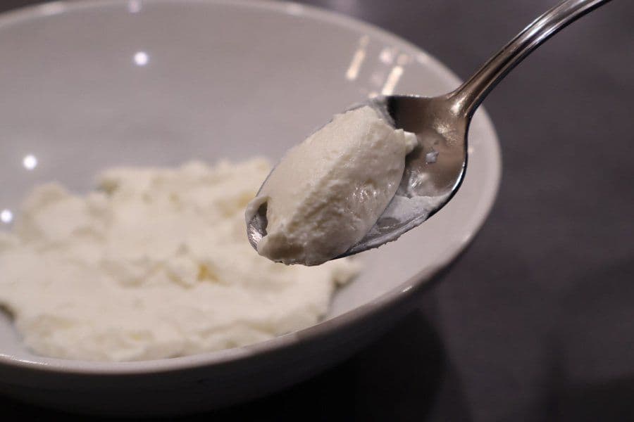 Spoon holding creamy hung curd above a bowl of strained yogurt.