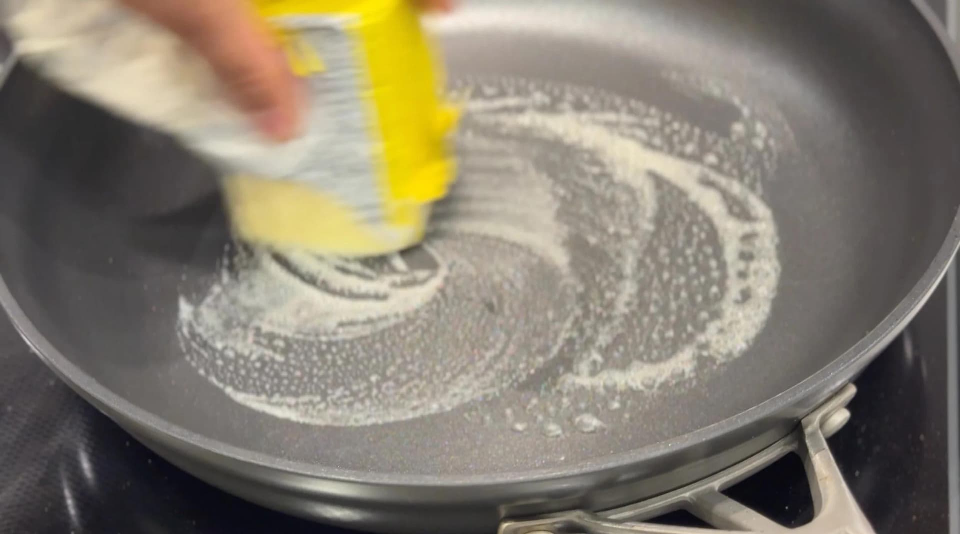 Butter being poured from a yellow container onto a heated pan with melting butter swirled across the surface.