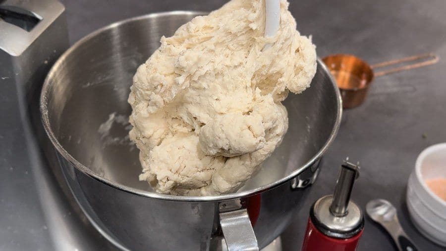 Pizza dough being kneaded in a stand mixer bowl, showing soft and pliable dough texture.