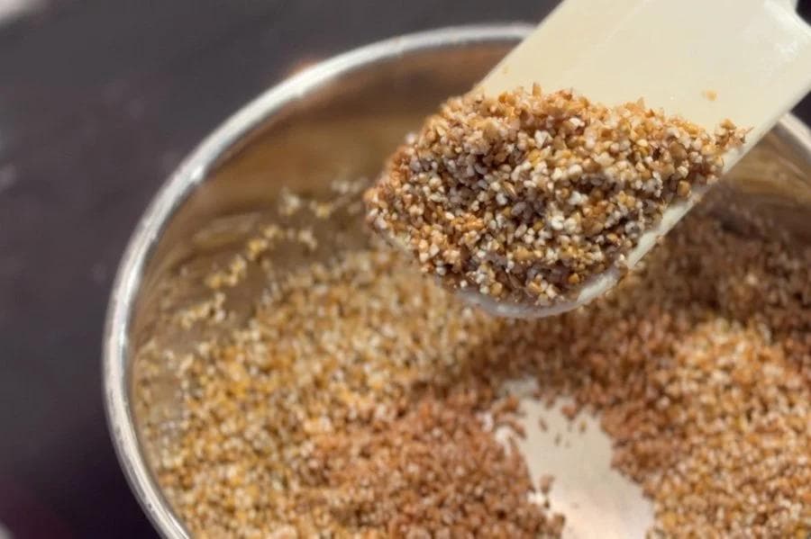 Cracked wheat being roasted in ghee in a saucepan until golden brown and aromatic.