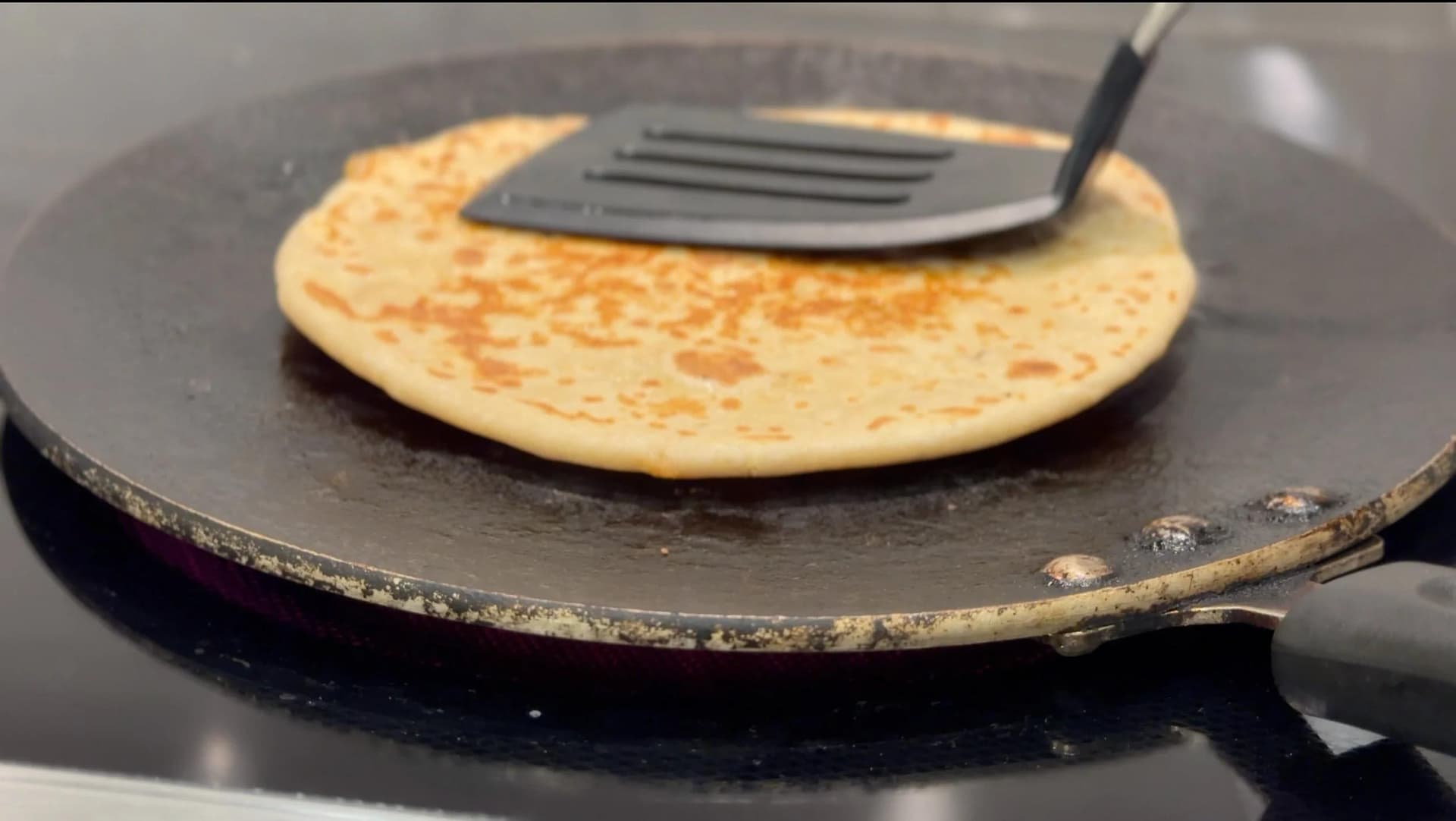 Cooked gobi paratha on a dark tawa with a spatula, showing golden-brown spots on the surface.