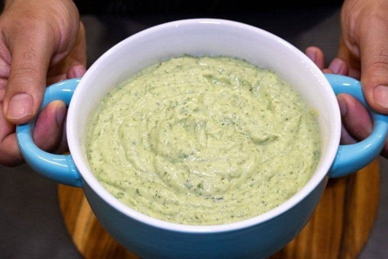 Creamy avocado lime crema in a blue and white bowl held by hands, ready to serve.